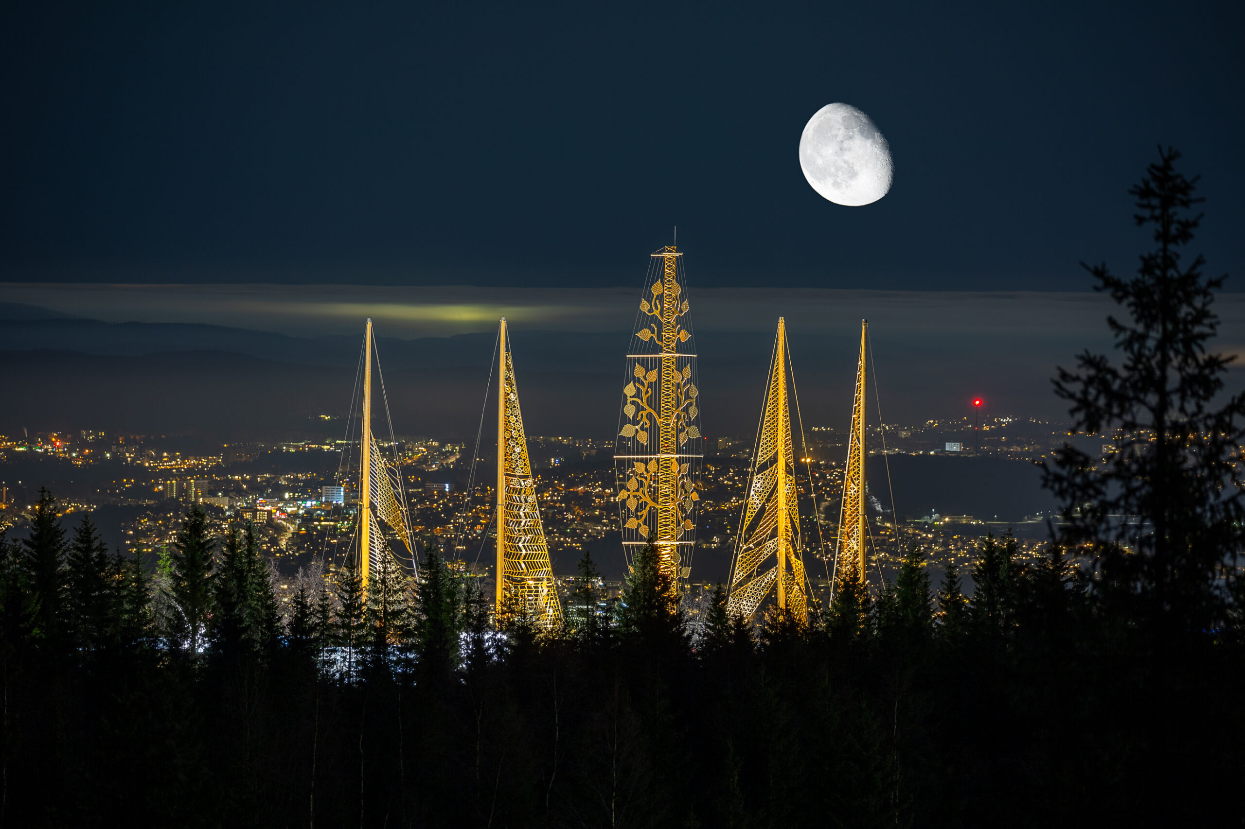 Kunstinstallasjonen Roseslottet ved Tryvann om kvelden, med gullbelagte master og Oslo i bakgrunnen